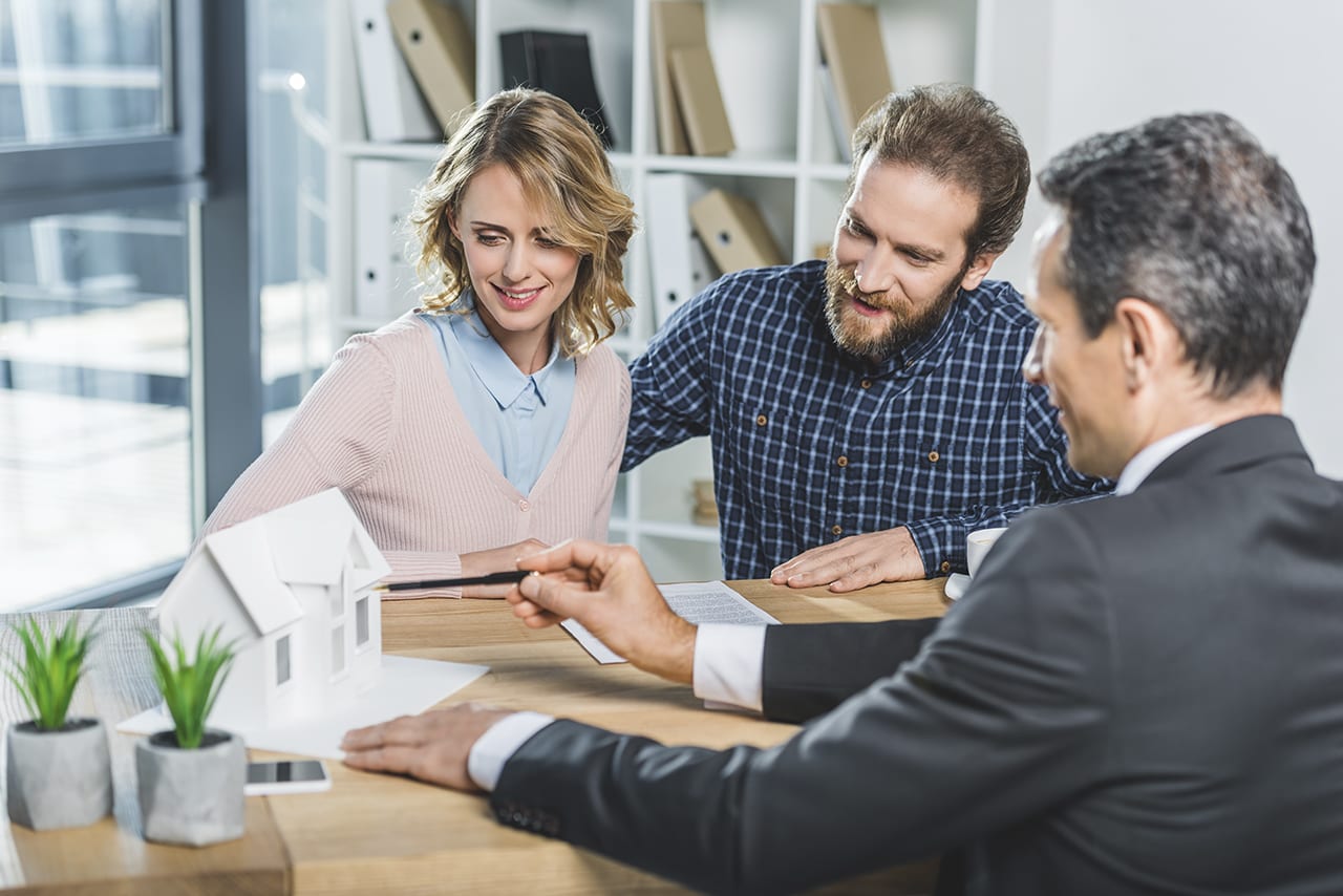 portrait of couple having meeting with realtor in real estate ag